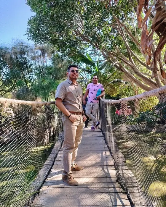 Rodolfo Gallegos en un puente colgante rodeado de vegetación en Africam Safari, con su amigo detrás