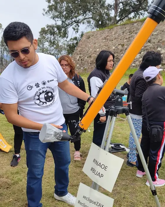 Rodolfo Gallegos junto a un telescopio con filtro solar, rodeado de asistentes, durante la observación de un eclipse en la zona arqueológica de Cacaxtla