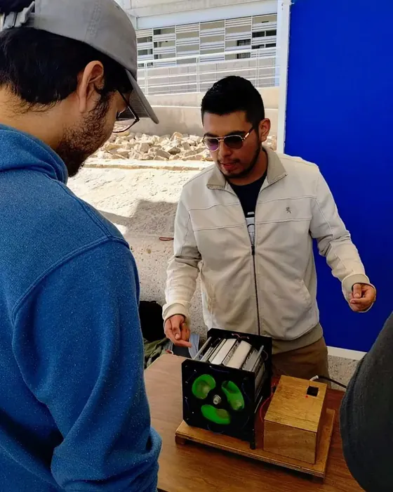 Rodolfo Gallegos explica un dispositivo electromagnético sobre una mesa a un asistente