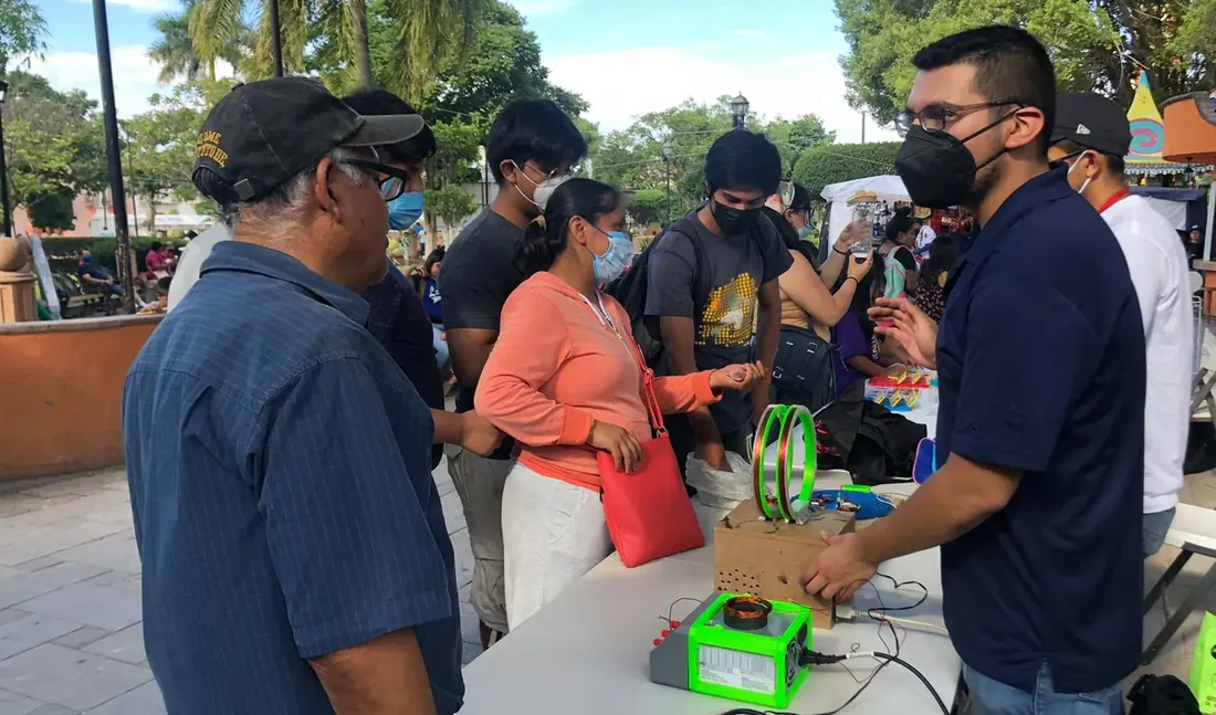 Rodolfo Gallegos con cubrebocas muestra un experimento de electricidad a varias personas en una plaza pública