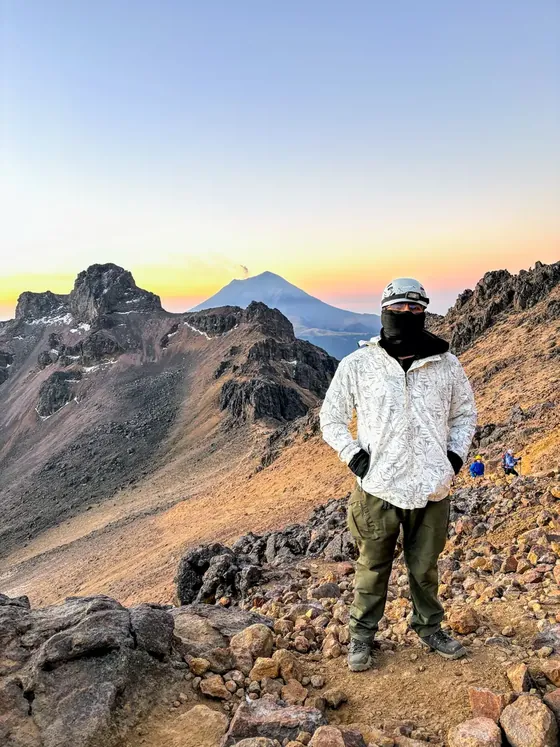 Rodolfo Gallegos con casco de montañismo en el Iztaccíhuatl al amanecer, con los Pies de la Mujer Dormida y el Popocatépetl al fondo